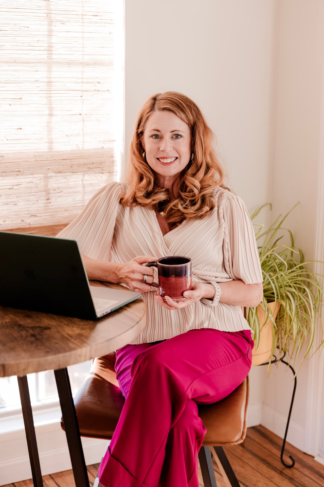 Tish, sitting at a sunlit table with her laptop and a coffee mug — warm, welcoming, ready to help.